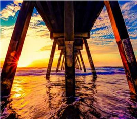 Foto van uitzicht op zee van onder een houten pier tijdens zons ondergang.